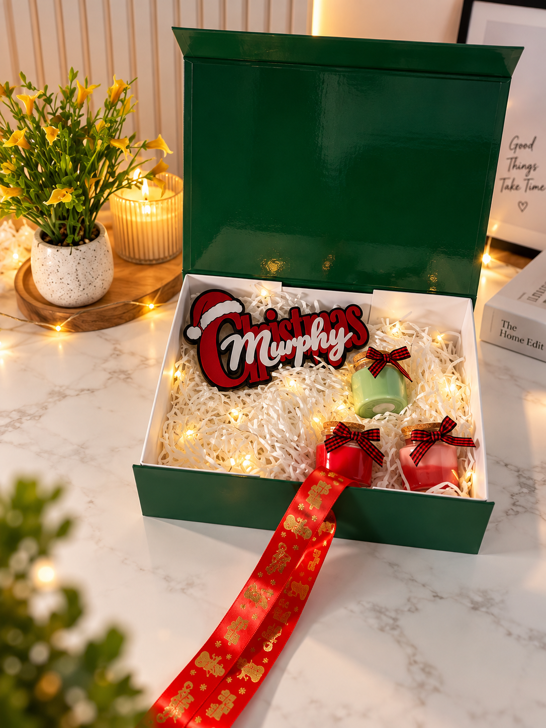 Personalised family Christmas gift kit with Murphy's name sign, scented candles and green magnetic gift box styled on marble table with fairy lights
